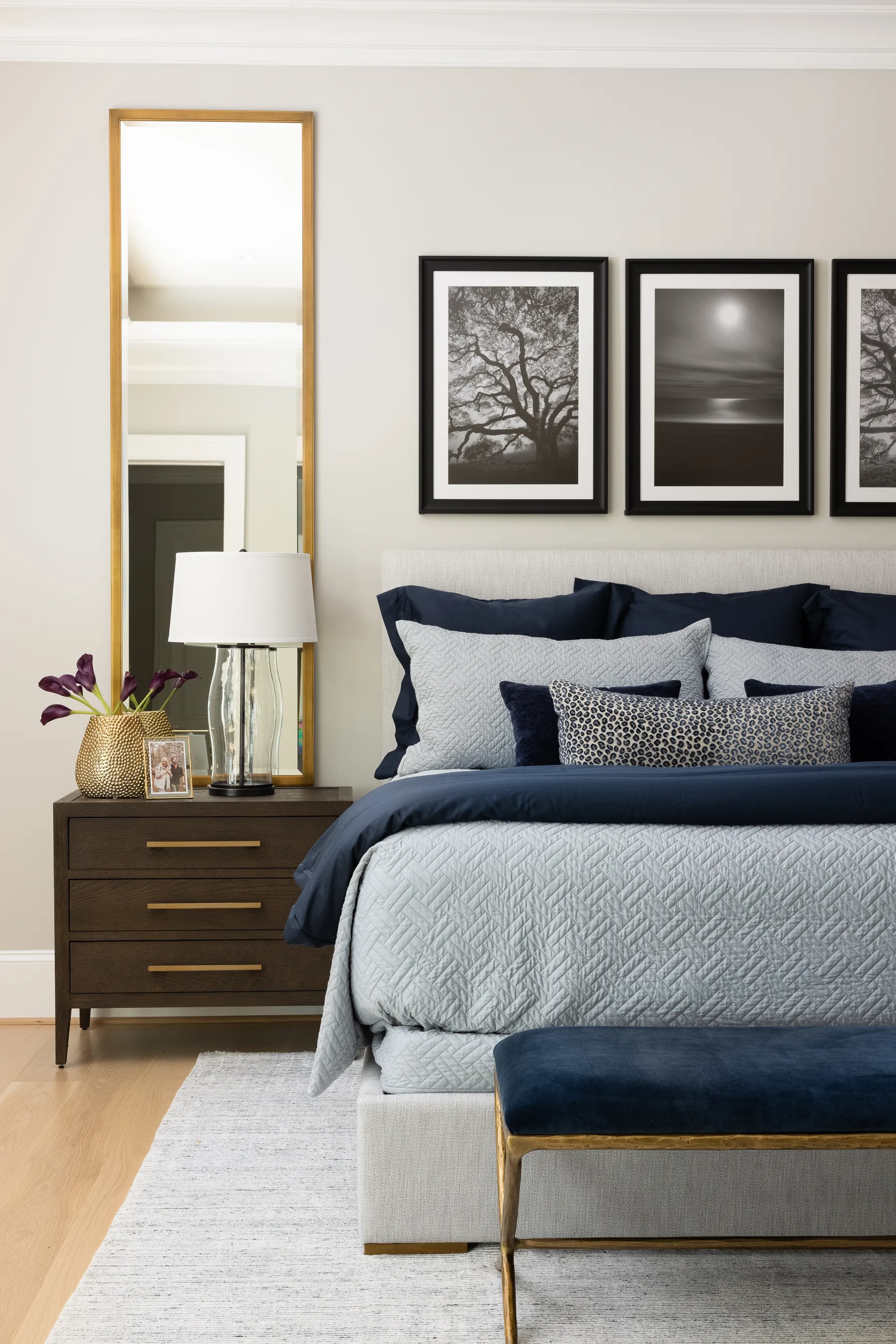 Layered bedding, a velvet bench and three framed photographs over the bed.
