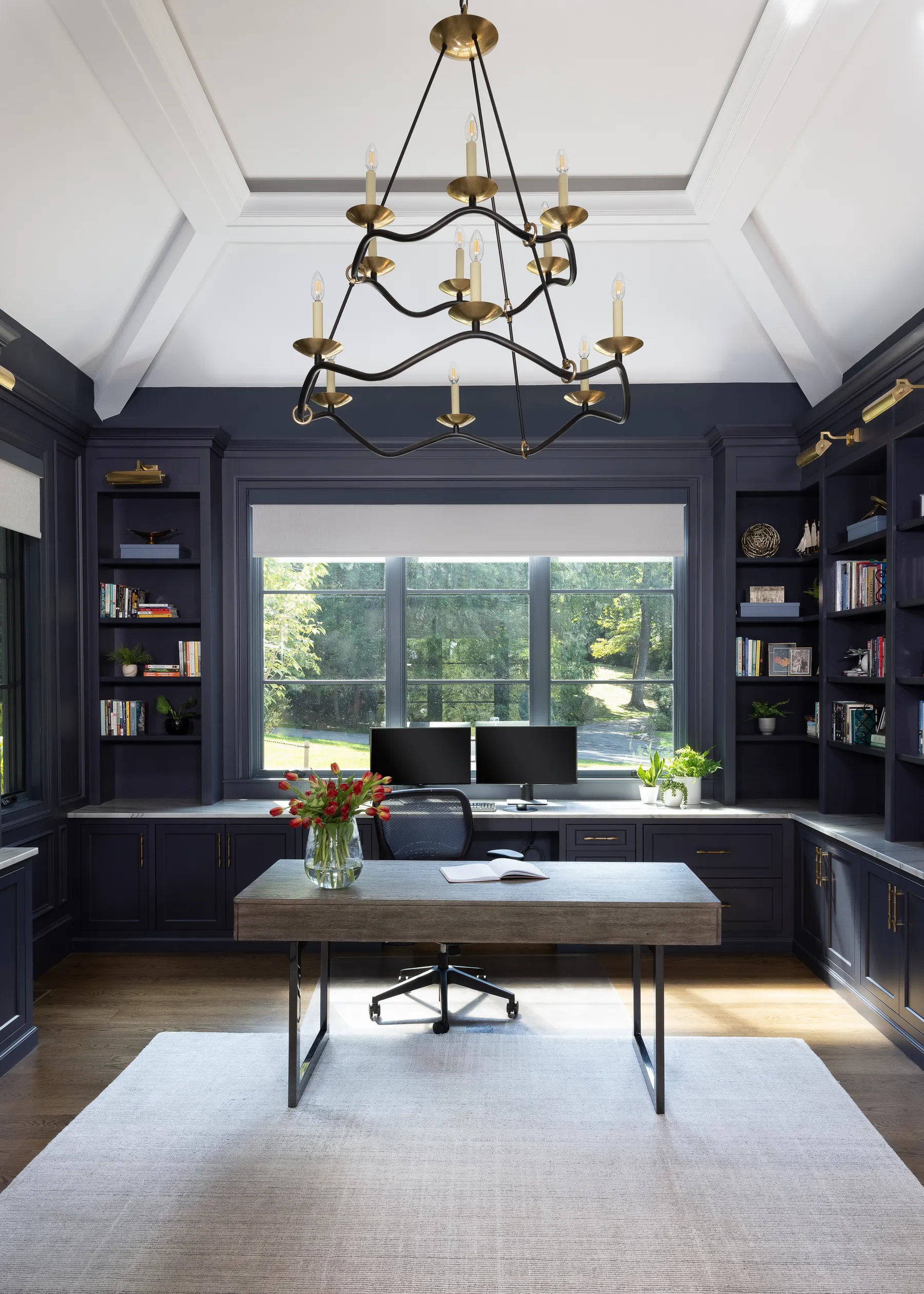 His office in deep navy, with built-in shelves and a brass chandelier.